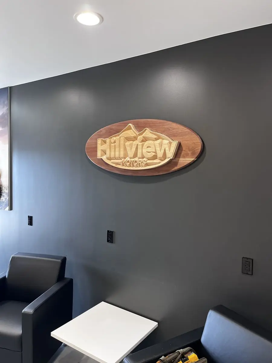 Carved oval Hillview Motors sign mounted on a dark gray wall in a lounge