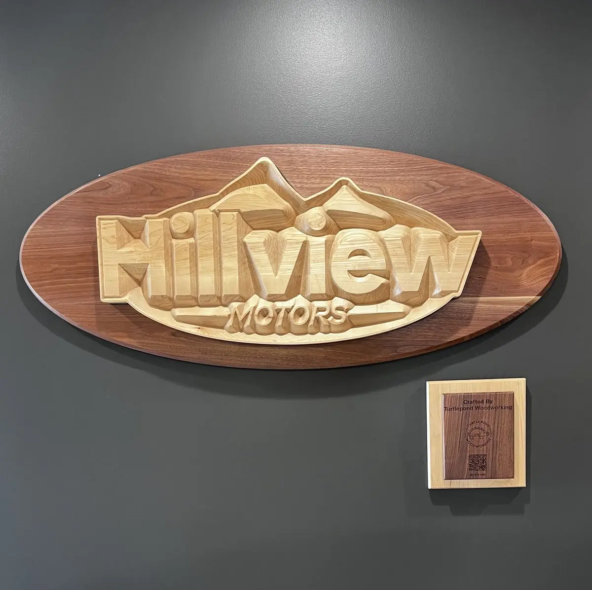 Carved oval wall sign reading Hillview Motors, with a small maker's plaque beside it