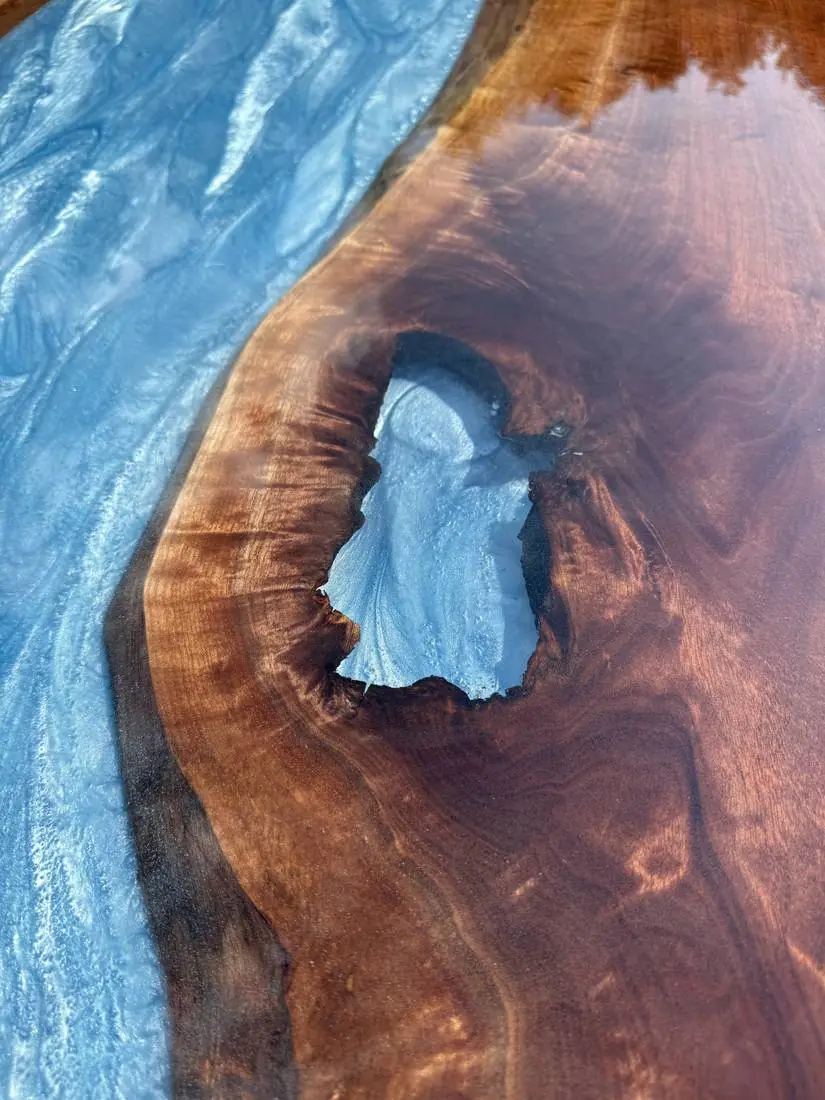Close-up of a blue epoxy river and a knot hole filled with epoxy in a glossy wood table top