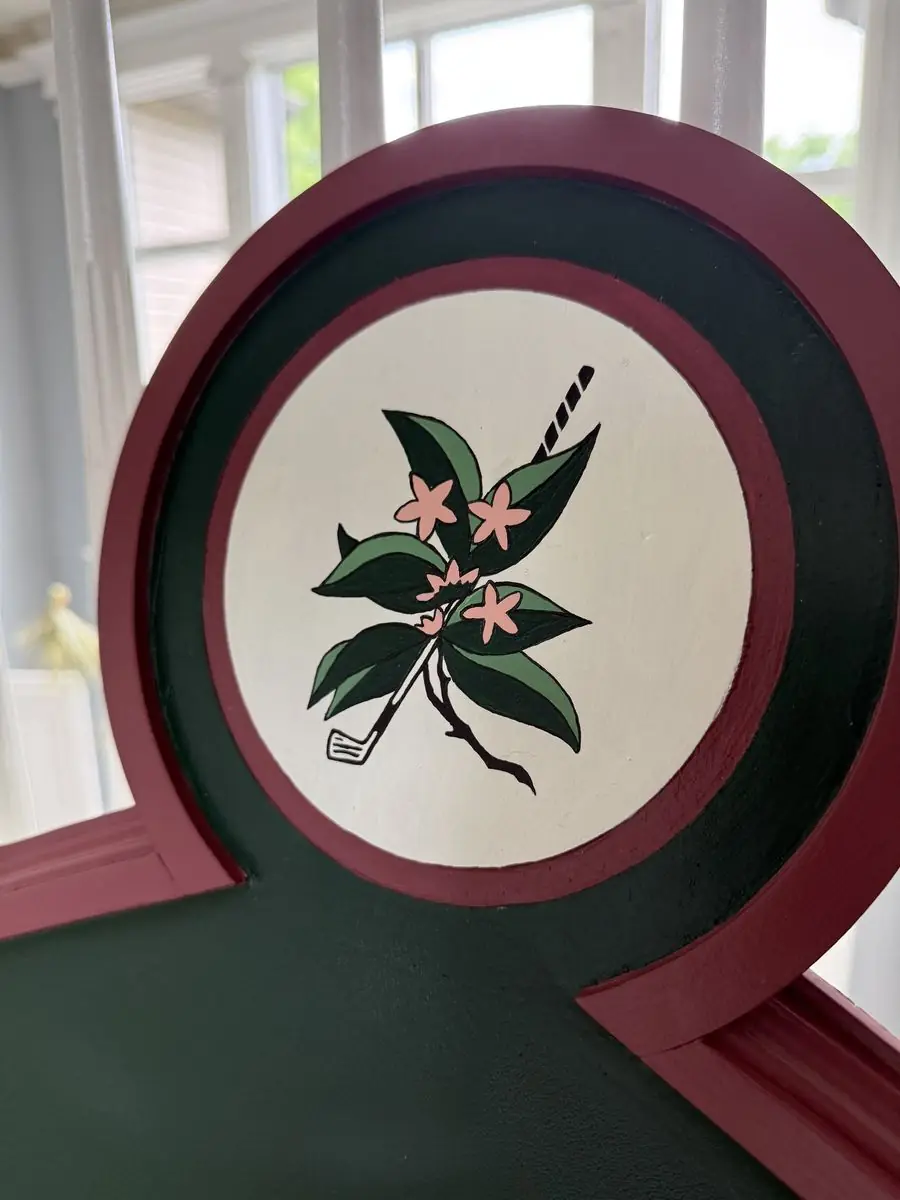 Close-up of a painted round emblem with pink blossoms and a golf club on a white field