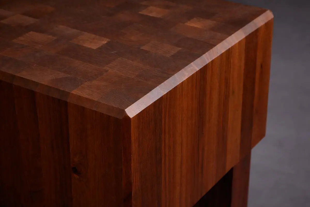 Close-up of the beveled corner of an end-grain butcher block top above a solid wood base
