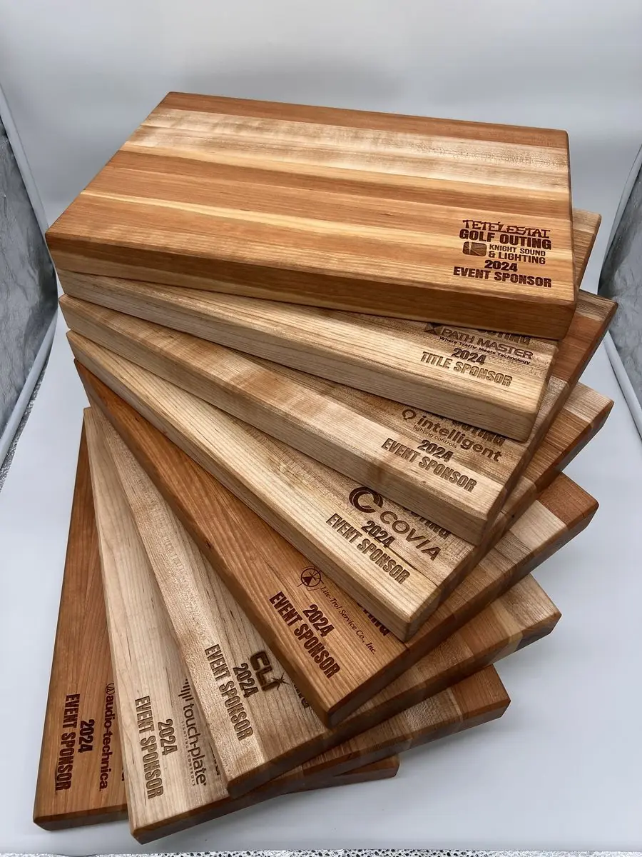Fanned stack of light and dark wood cutting boards, each engraved with a sponsor logo and the words 2024 Event Sponsor