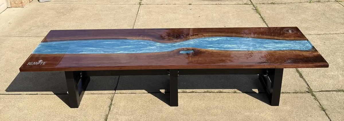 Long wooden river table with a blue epoxy river and black steel legs, on a driveway