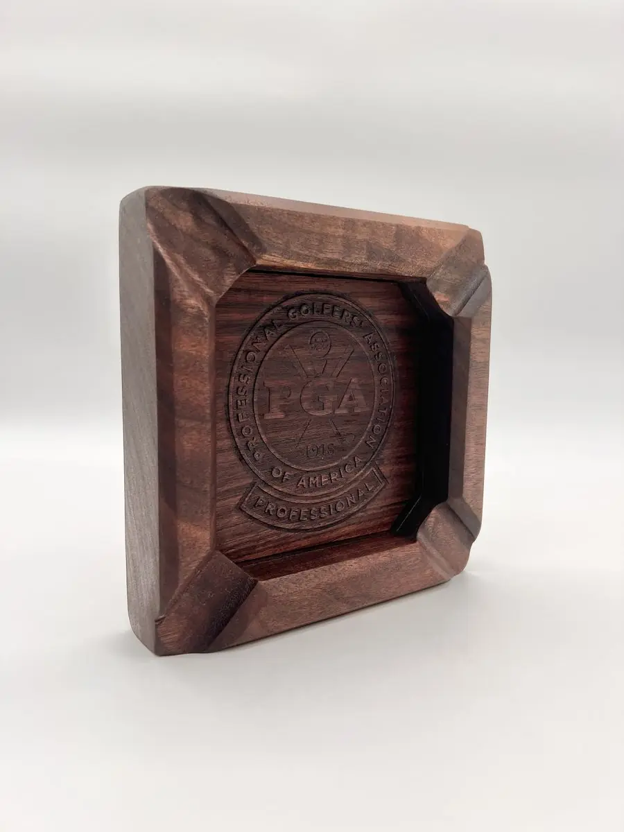 Square dark wood ashtray with an engraved PGA seal, seen at an angle