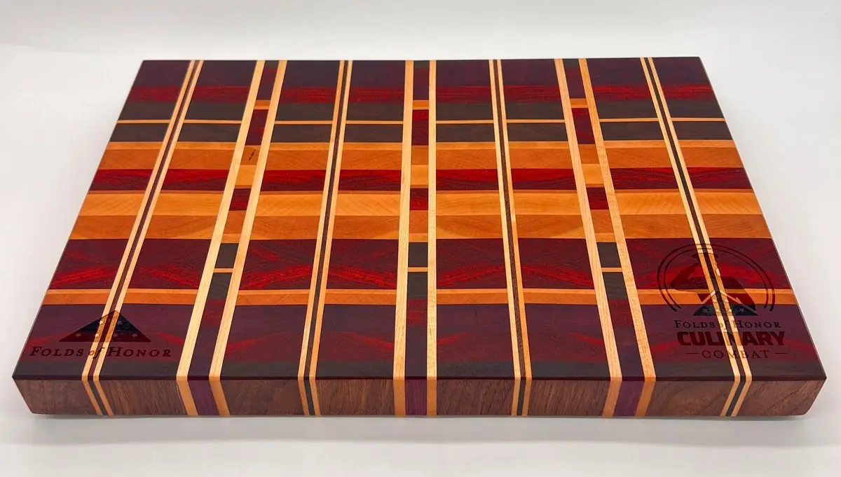 Striped end-grain cutting board in red, orange, purple and dark woods with engraved logos in two corners