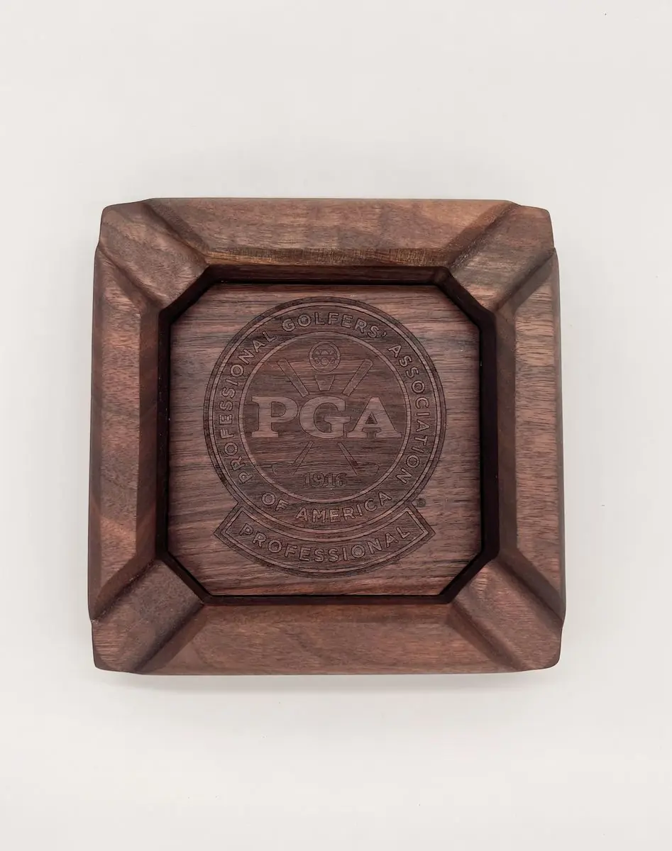 Top view of a square dark wood ashtray with an engraved PGA seal