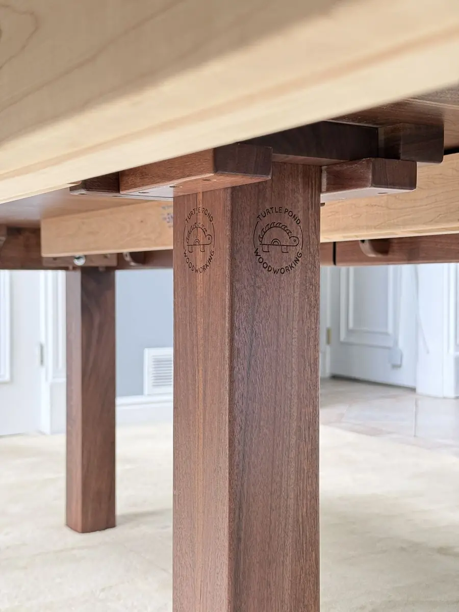 Underside of a table showing an engraved Turtle Pond Woodworking logo on a leg