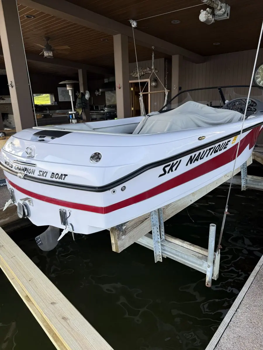 White Ski Nautique ski boat with glossy red and black graphics, raised on a boat lift in a covered boathouse