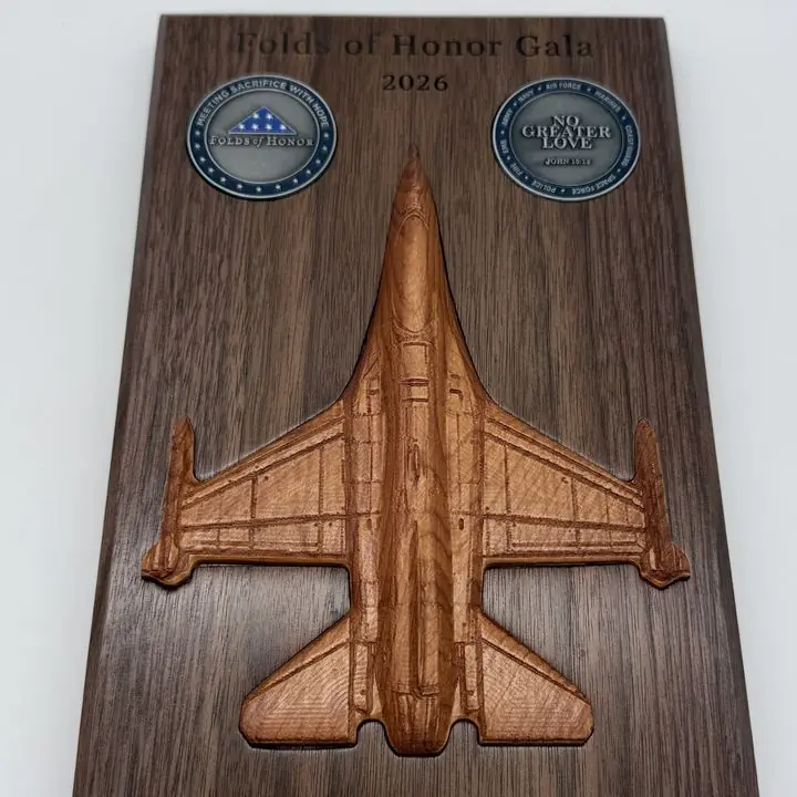 Wooden plaque with a carved fighter jet, two challenge coins and engraved text for a charity gala